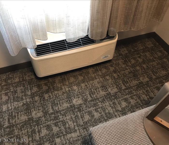 Air conditioning unit in hotel room with carpet floor.