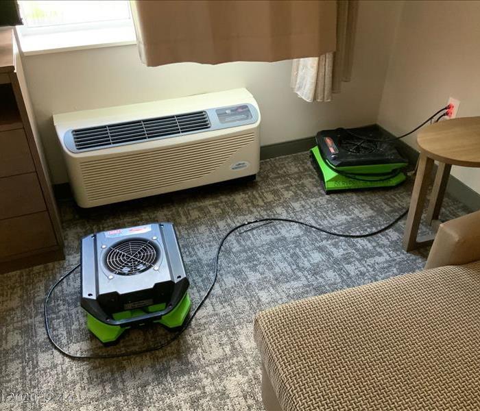 Air conditioning unit in hotel room with air movers set up on the carpet around it. 
