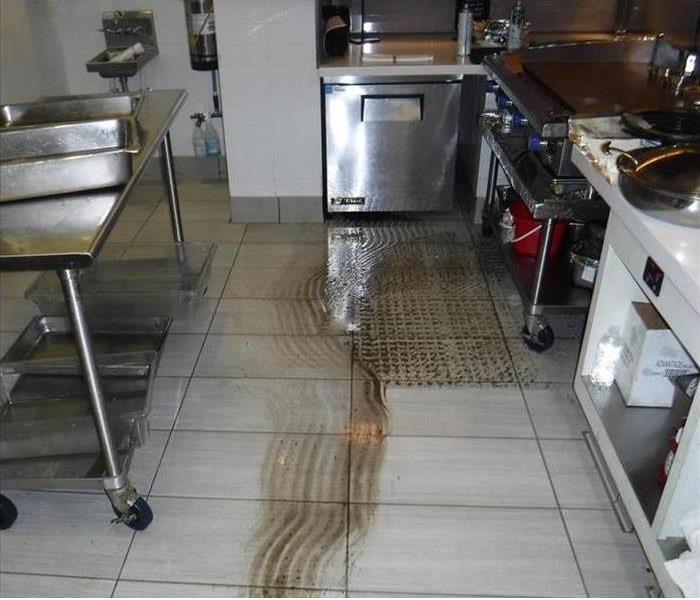 Brown water collected on white tile floor of commercial kitchen.