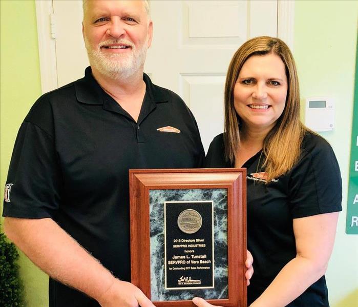 Man and woman posed together holding a SERVPRO award placard.